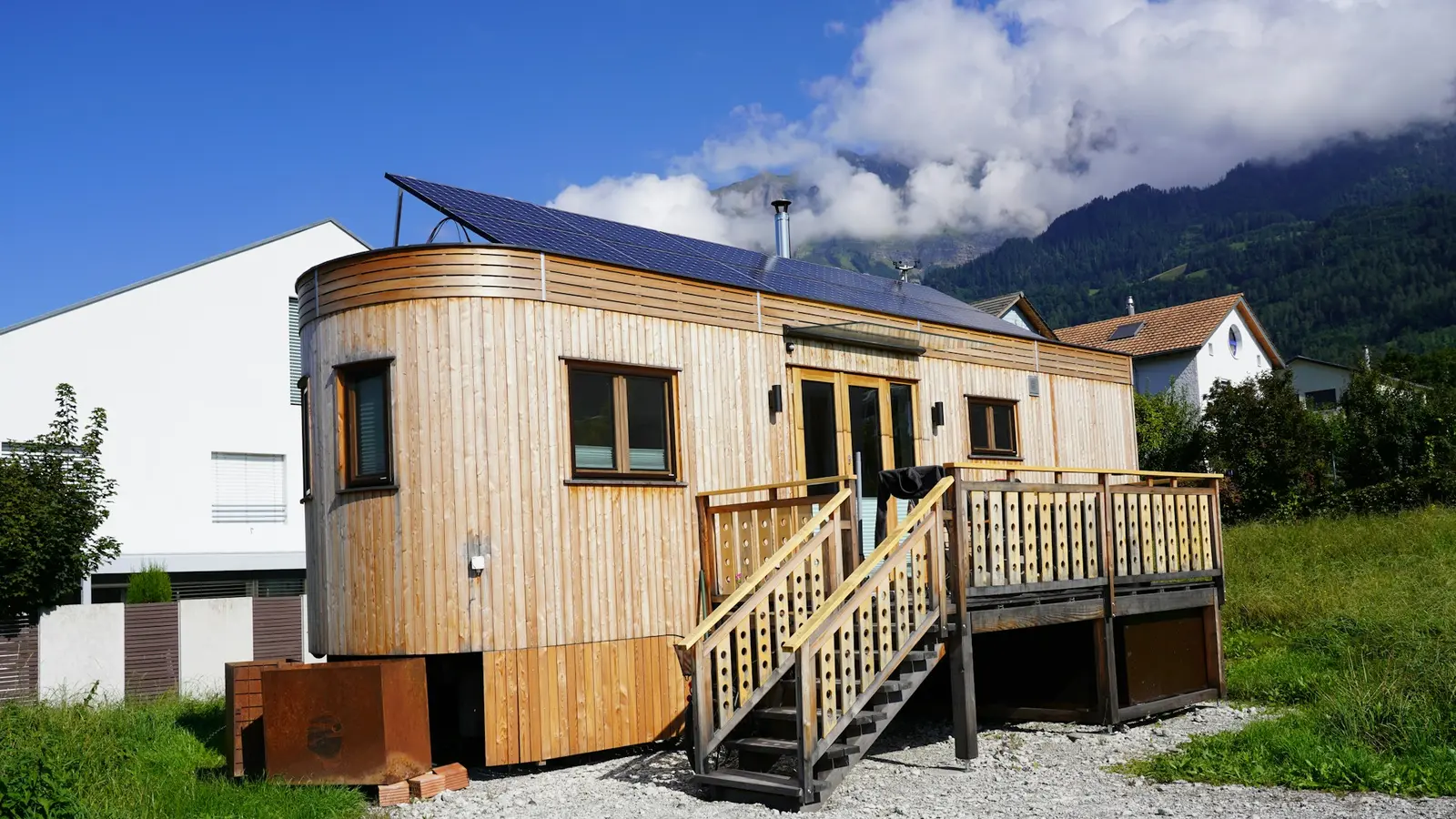 Tiny house placată cu lemn, cu terasă și scară, pe pietriș